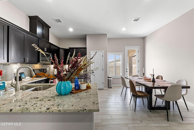 kitchen featuring visible vents, decorative backsplash, light stone counters, stainless steel microwave, and a sink