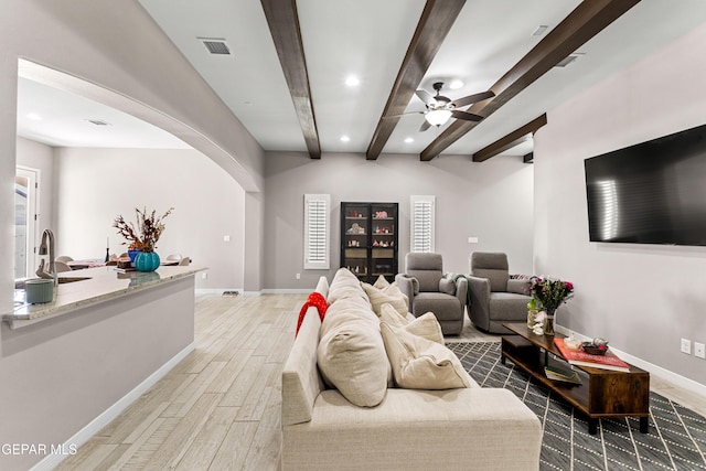 living room with arched walkways, visible vents, baseboards, light wood-type flooring, and beamed ceiling