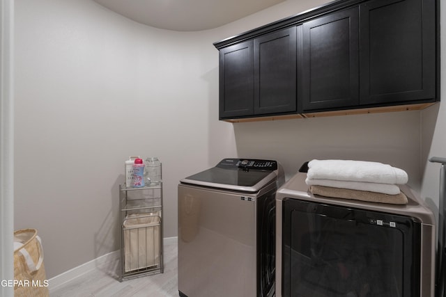 washroom featuring light wood finished floors, washing machine and dryer, cabinet space, and baseboards