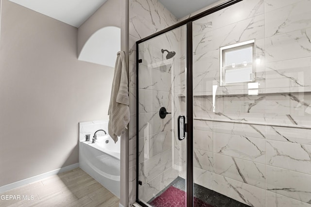 bathroom featuring wood finished floors, a marble finish shower, a bath, and baseboards