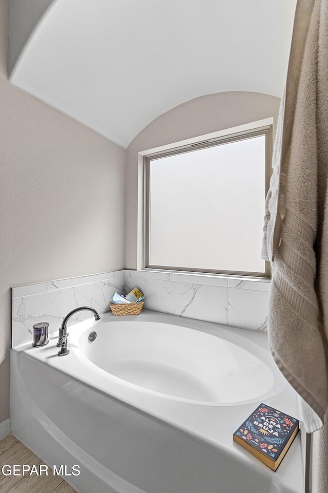 bathroom with lofted ceiling, wood finished floors, and a garden tub