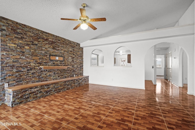 unfurnished living room with a textured ceiling, ceiling fan, arched walkways, lofted ceiling, and baseboards