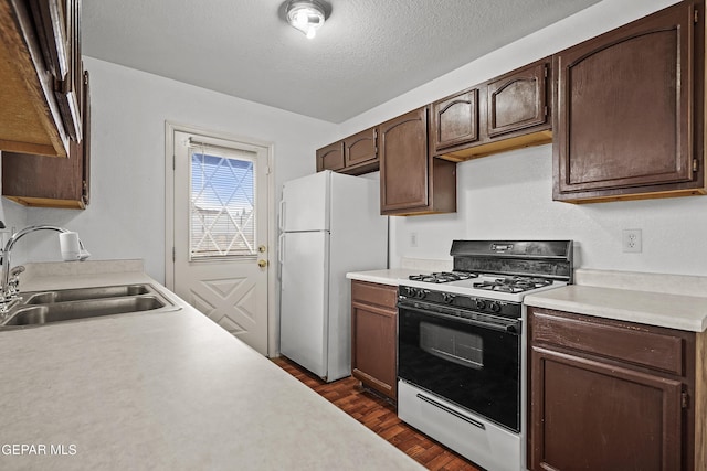 kitchen with dark wood-style flooring, freestanding refrigerator, gas range oven, light countertops, and a sink