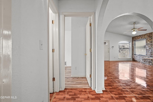 corridor featuring arched walkways, a textured ceiling, and baseboards