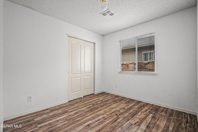 empty room featuring a textured ceiling, wood finished floors, visible vents, and baseboards