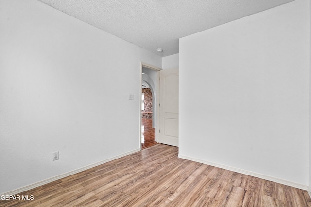 unfurnished room with light wood-type flooring, baseboards, arched walkways, and a textured ceiling