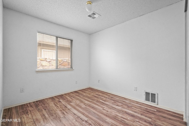 unfurnished room with a textured ceiling, wood finished floors, visible vents, and baseboards