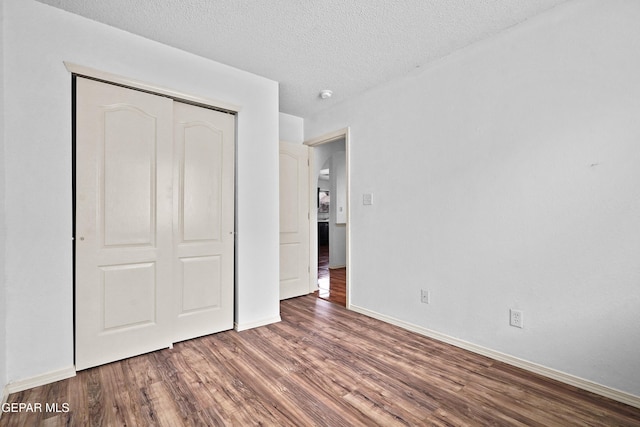 unfurnished bedroom featuring a textured ceiling, a closet, baseboards, and wood finished floors