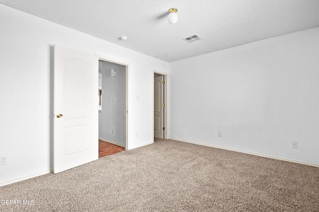 empty room featuring a textured ceiling, carpet, visible vents, and baseboards