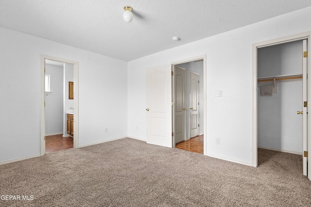 unfurnished bedroom featuring a textured ceiling, carpet floors, a closet, and a walk in closet