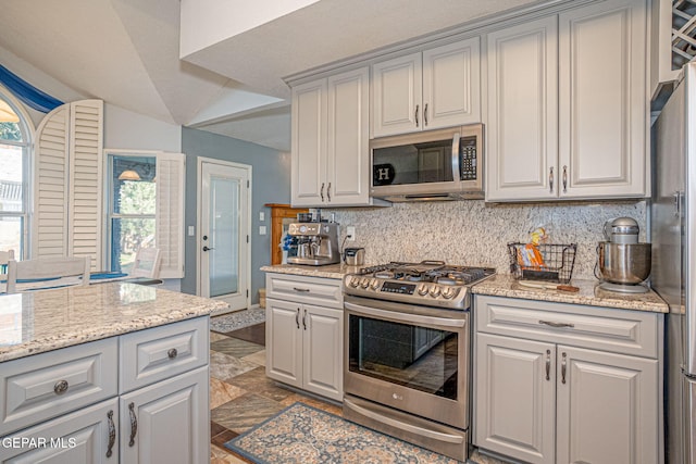 kitchen featuring stone finish floor, appliances with stainless steel finishes, light stone counters, and backsplash