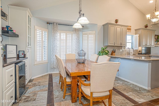 dining space featuring high vaulted ceiling, beverage cooler, baseboards, stone finish flooring, and an inviting chandelier