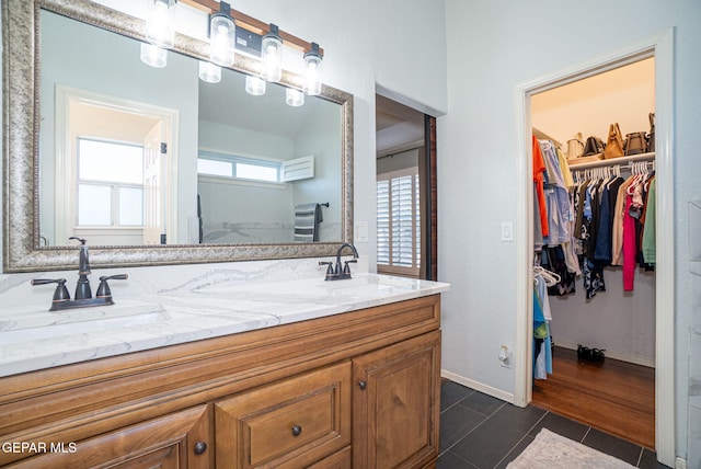 full bathroom featuring double vanity, a spacious closet, a sink, baseboards, and tile patterned floors