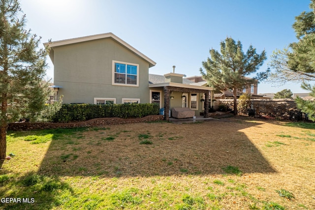 back of house featuring fence, a lawn, and stucco siding