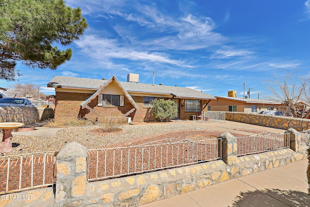 view of front of home with a fenced front yard, concrete driveway, brick siding, and roof with shingles