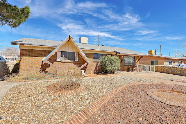 view of front facade with a shingled roof, brick siding, a patio, and fence