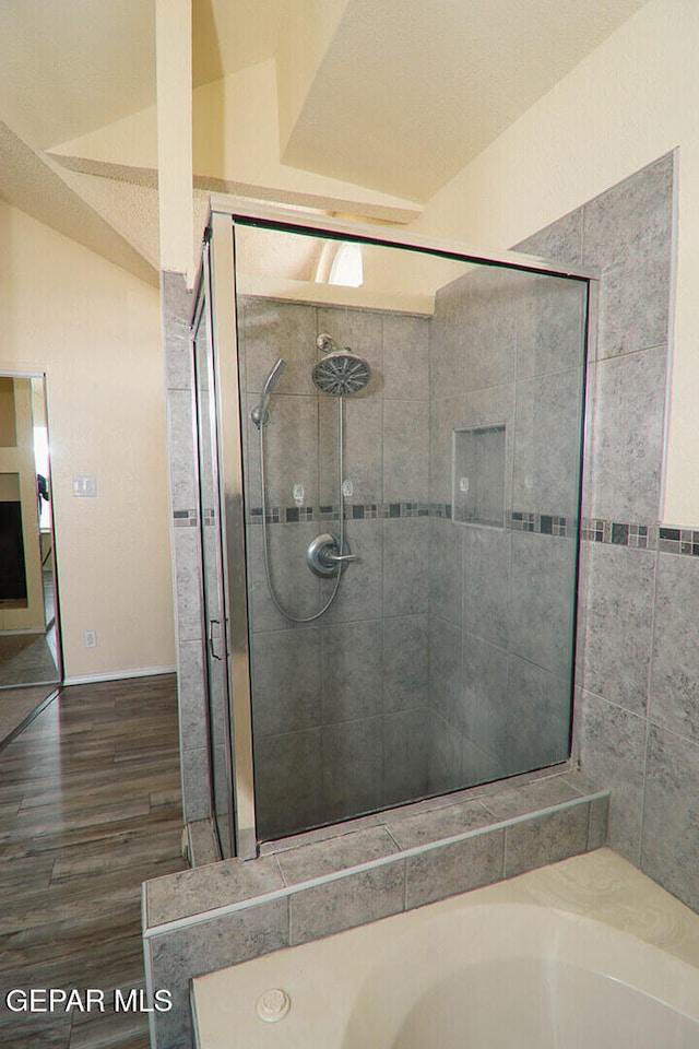 bathroom featuring lofted ceiling, wood finished floors, a shower stall, and a washtub