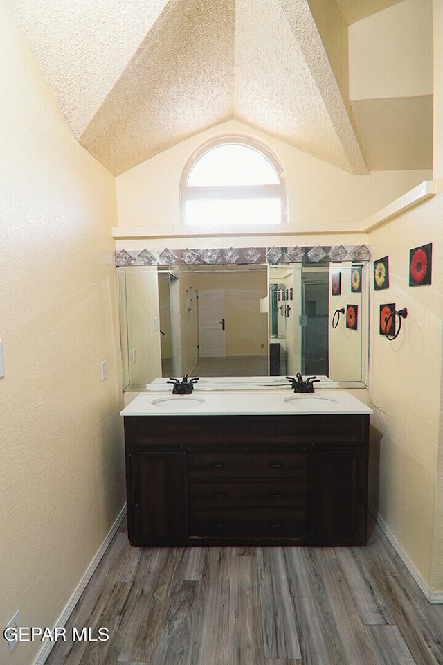 bathroom featuring vaulted ceiling, a textured ceiling, a sink, and wood finished floors