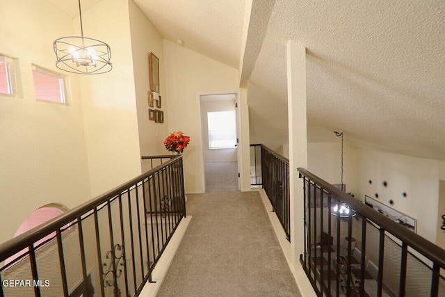 hall with a notable chandelier, light carpet, vaulted ceiling, a textured ceiling, and an upstairs landing