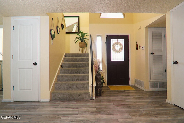 entrance foyer featuring a textured ceiling, stairs, visible vents, and wood finished floors