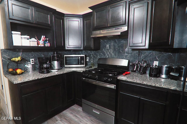 kitchen with stainless steel microwave, gas range oven, backsplash, and under cabinet range hood