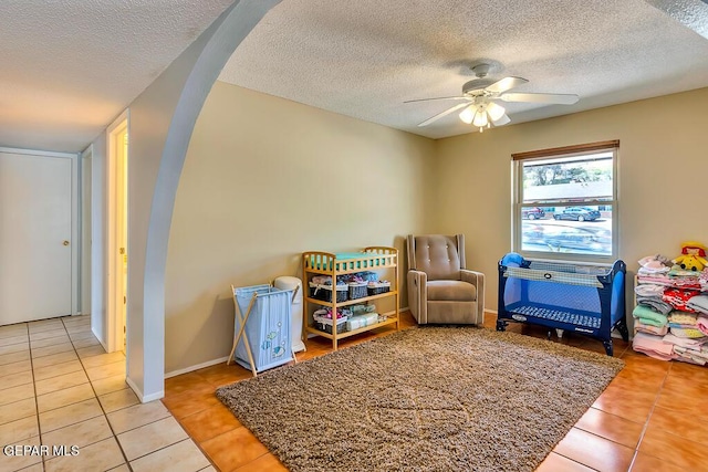 playroom with arched walkways, tile patterned flooring, a textured ceiling, and ceiling fan