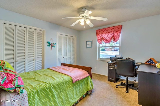 bedroom with a textured ceiling, a ceiling fan, two closets, and light carpet