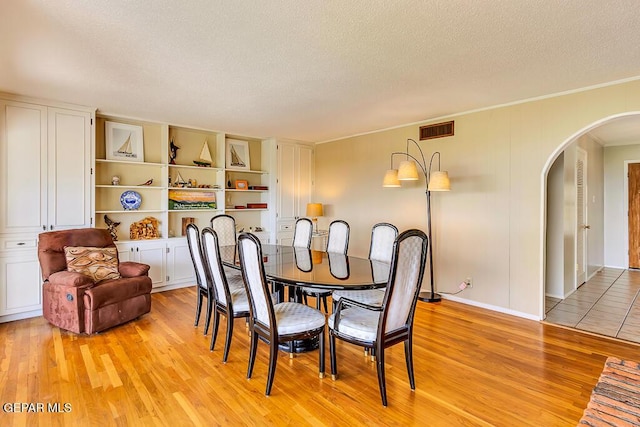 dining space featuring visible vents, a textured ceiling, arched walkways, crown molding, and light wood finished floors