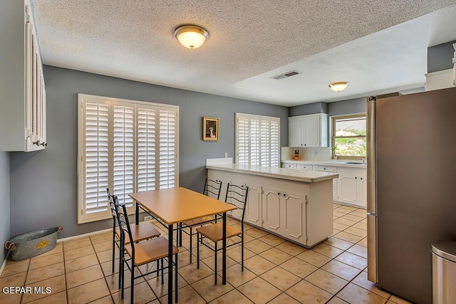 kitchen with visible vents, light countertops, light tile patterned floors, freestanding refrigerator, and white cabinetry