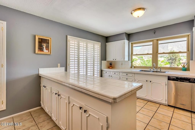 kitchen with a sink, stainless steel dishwasher, white cabinetry, light tile patterned floors, and tile counters