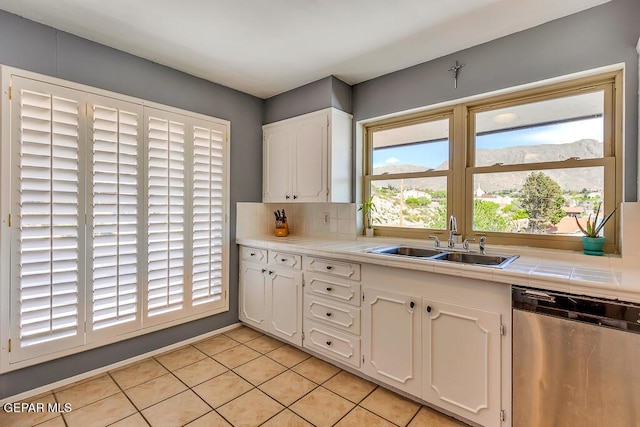 kitchen featuring tasteful backsplash, tile countertops, stainless steel dishwasher, white cabinetry, and a sink