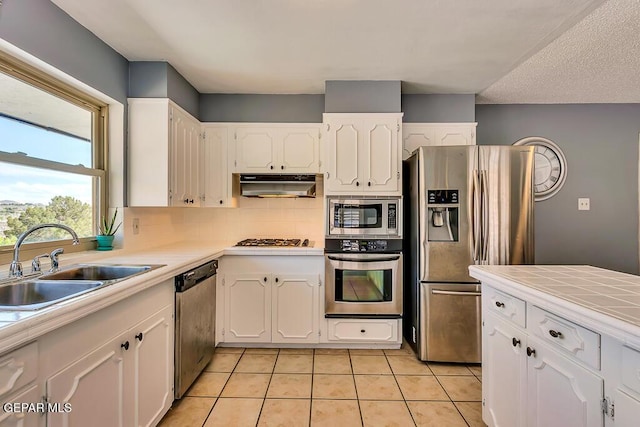 kitchen featuring under cabinet range hood, a sink, appliances with stainless steel finishes, white cabinets, and light tile patterned floors