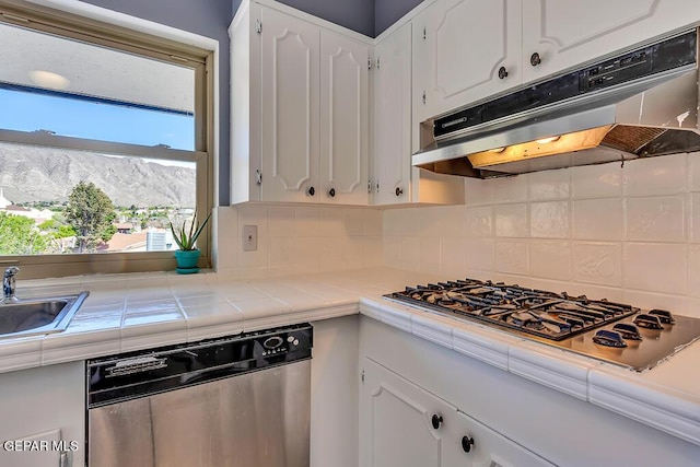 kitchen with tile countertops, stainless steel appliances, under cabinet range hood, white cabinetry, and backsplash