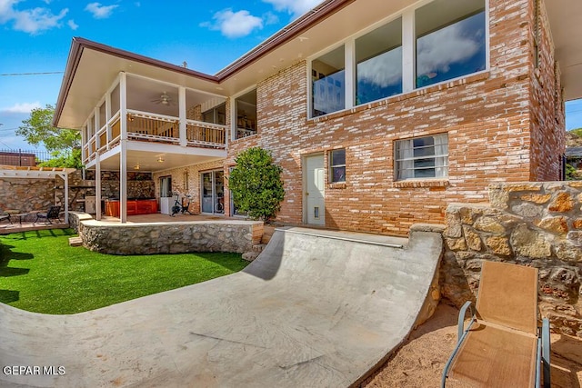 rear view of property with a balcony, a ceiling fan, a lawn, a patio area, and brick siding