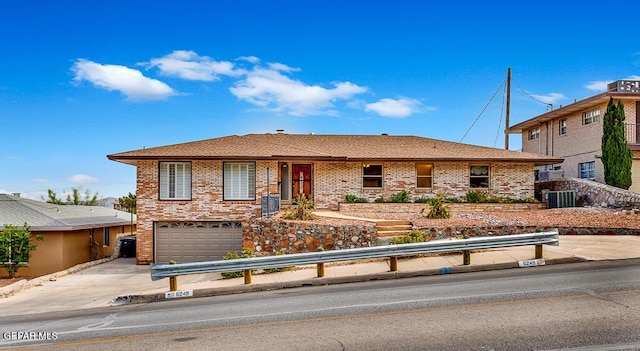 ranch-style home with driveway, roof with shingles, an attached garage, brick siding, and central AC unit