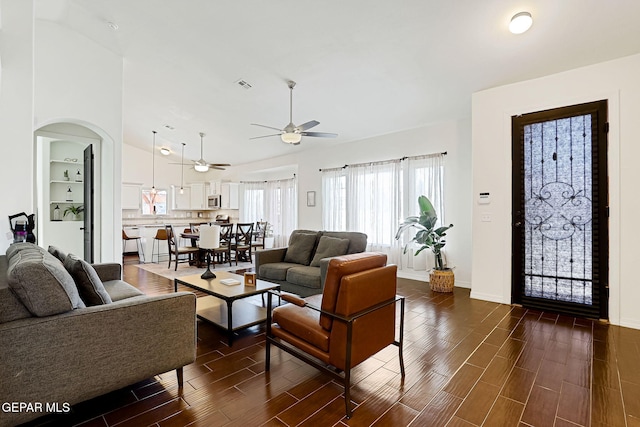 living room with visible vents, wood tiled floor, lofted ceiling, arched walkways, and ceiling fan