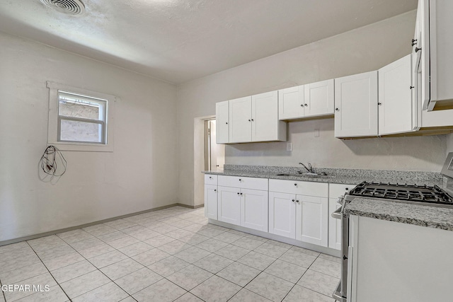 kitchen with visible vents, white cabinets, light stone counters, stainless steel gas range, and a sink