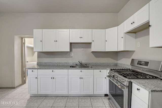 kitchen featuring light tile patterned floors, gas stove, white cabinetry, a sink, and light stone countertops