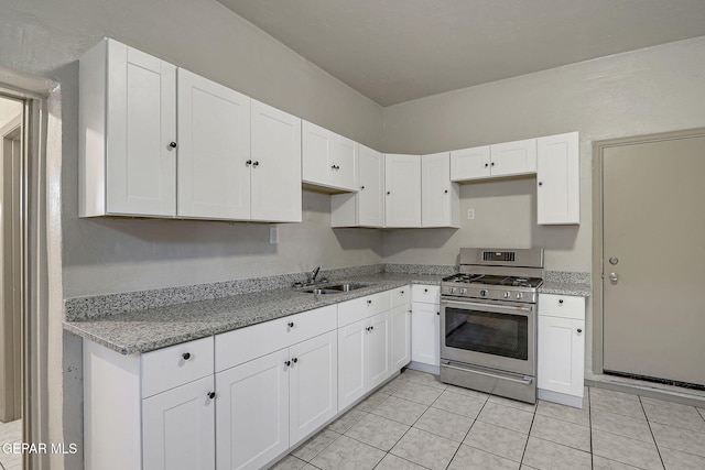 kitchen with light tile patterned flooring, a sink, white cabinets, light stone countertops, and gas range