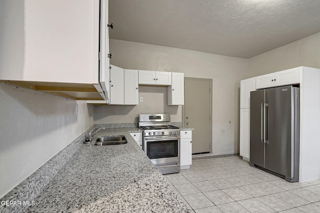 kitchen with light stone counters, light tile patterned flooring, stainless steel appliances, a sink, and white cabinetry