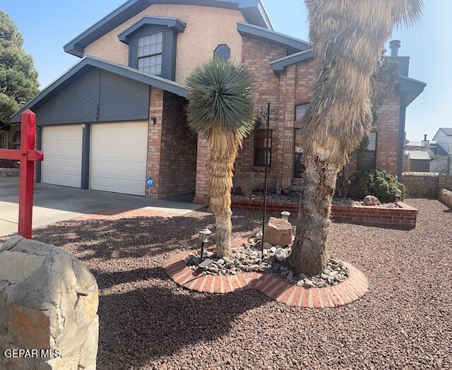 view of front of property with an attached garage, stucco siding, driveway, and brick siding