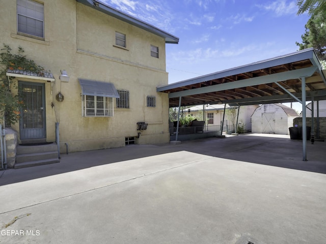 exterior space featuring concrete driveway, an outbuilding, a storage unit, a carport, and stucco siding