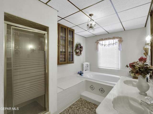 bathroom with a bath, a stall shower, a paneled ceiling, and an inviting chandelier