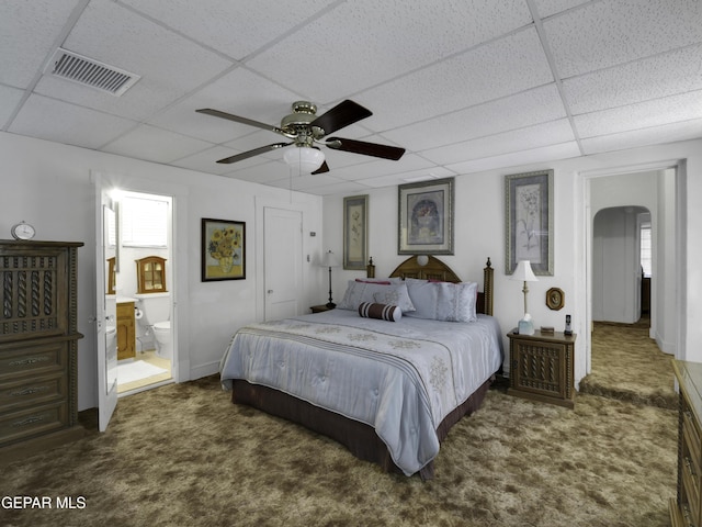 carpeted bedroom with arched walkways, connected bathroom, a paneled ceiling, visible vents, and baseboards