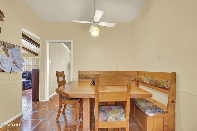 tiled dining area with a wainscoted wall and ceiling fan