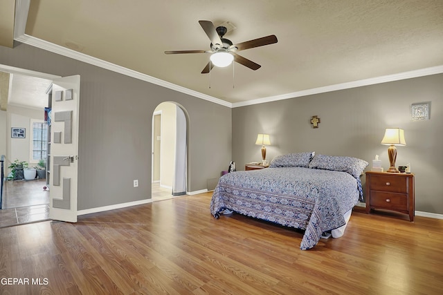 bedroom featuring baseboards, crown molding, arched walkways, and wood finished floors