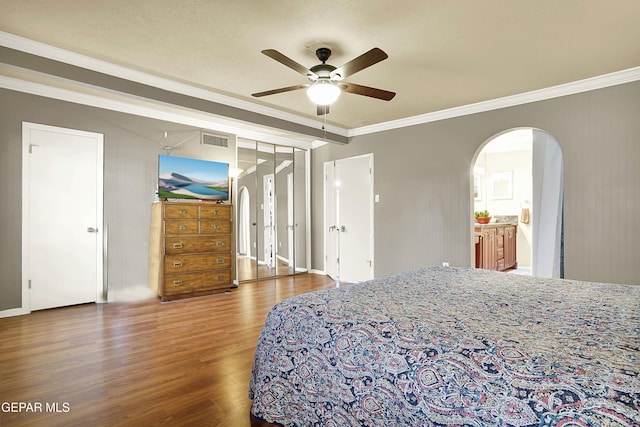 bedroom with arched walkways, wood finished floors, visible vents, and crown molding