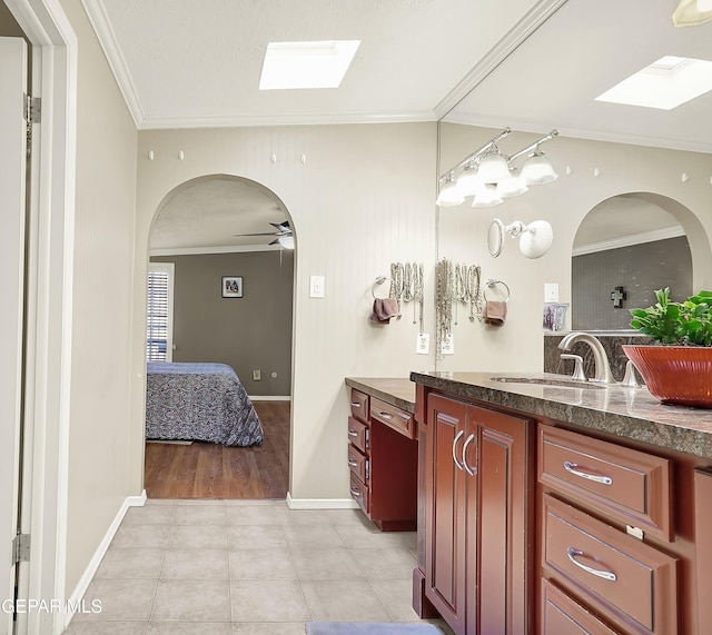 bathroom with a skylight, crown molding, ceiling fan, vanity, and tile patterned flooring