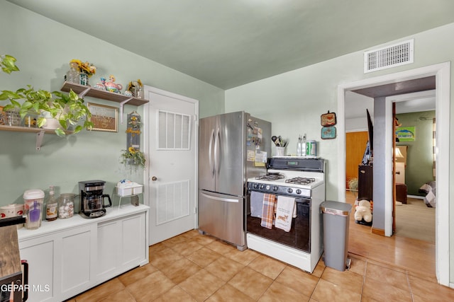 kitchen featuring visible vents, white gas range oven, freestanding refrigerator, and white cabinetry