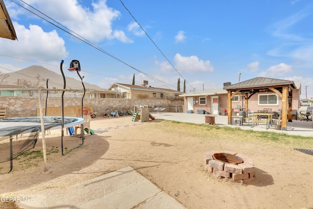 view of yard featuring a fire pit, a trampoline, fence, a gazebo, and a patio area